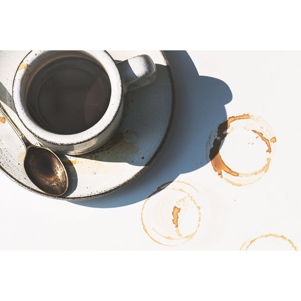 Cup of coffee with a spoon on a white surface with coffee stains.